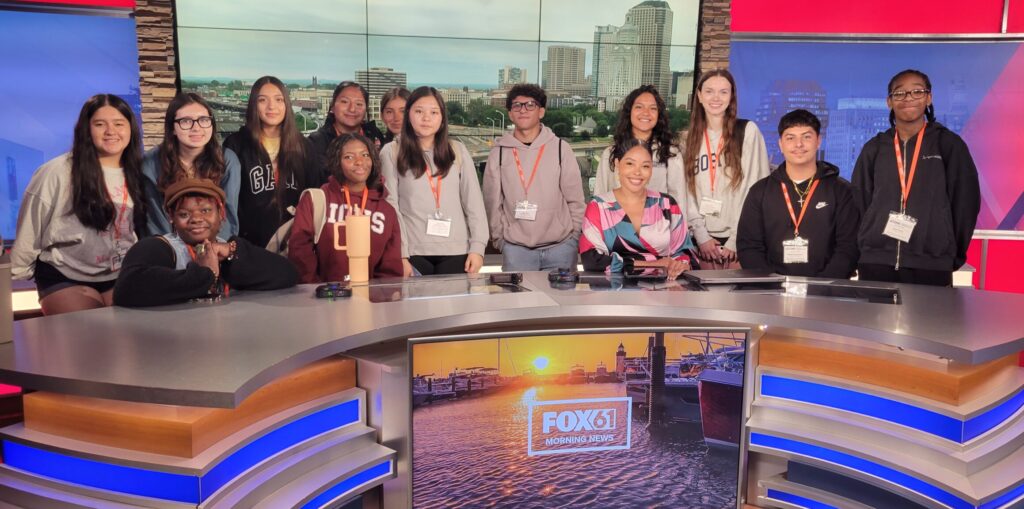 Students spent half a day visiting the FOX 61 studio in Hartford to see what goes into a news show, work the weather green screen and meet the morning news crew. Here, students pose with anchor Symphonie Privett. / Photo by Julie Serkosky