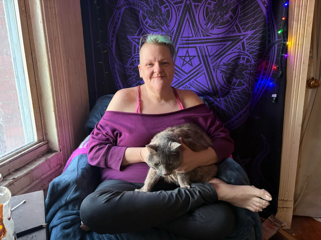 A woman in a purple shirt holding a gray cat in her lap.